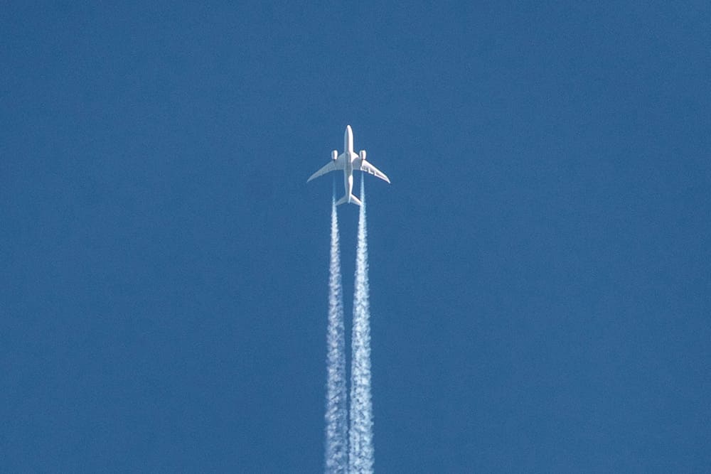 青空を飛行する旅客機と飛行機雲を捉えた写真。8月の海外旅行をおトクに楽しむためのヒントを紹介するセクションのイメージビジュアルに最適