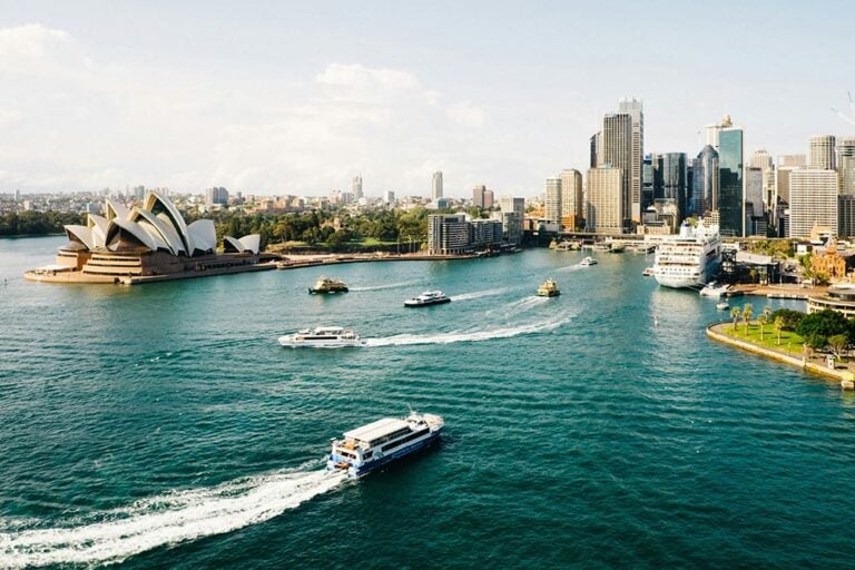 8月のシドニー湾に浮かぶフェリーと、オペラハウスと高層ビル群が並ぶ景観