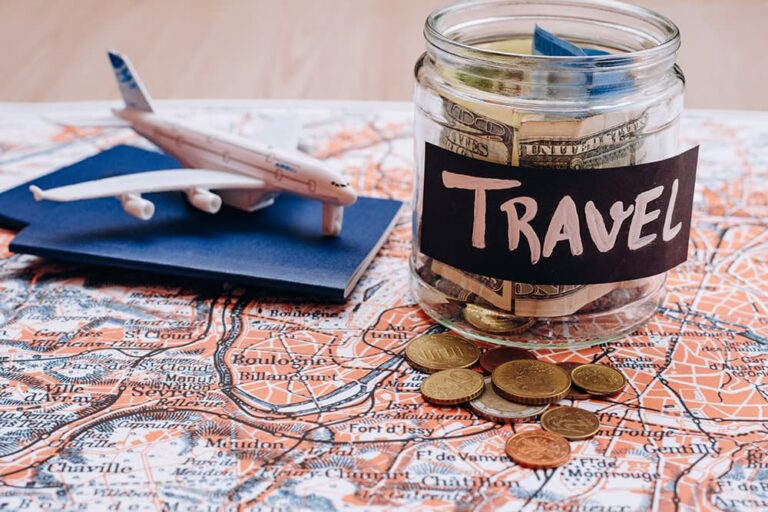 地図の上に置かれた「TRAVEL」と書かれた貯金瓶とパスポート・飛行機の模型・コインの俯瞰