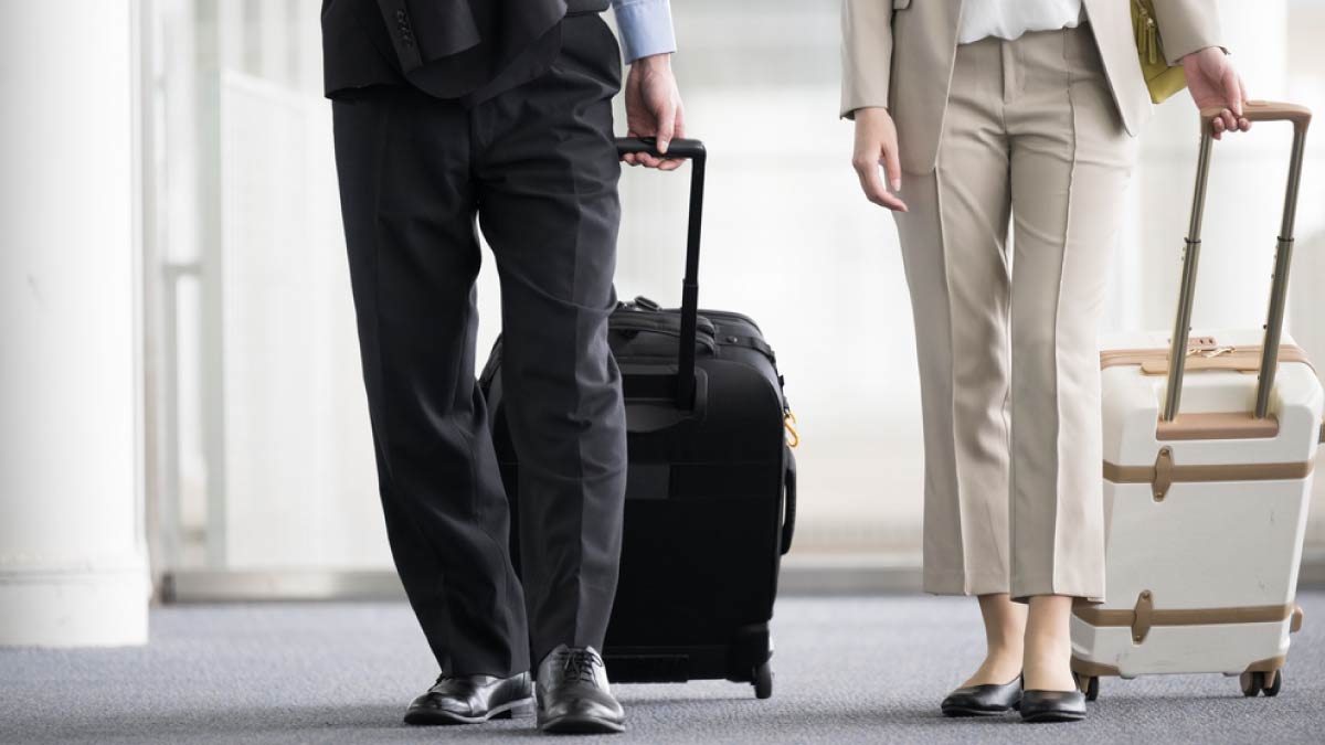 スーツケースを引きながら空港内を歩くスーツ姿の男女。ビジネス出張中の様子を捉えた一場面。