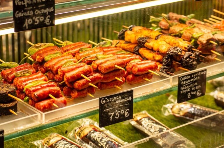 スペイン・マドリードの市場で売られているチストラ（Chistorra）や串焼き料理。色とりどりのピンチョスがガラスケースに並び、活気あるスペインの食文化を感じられる。