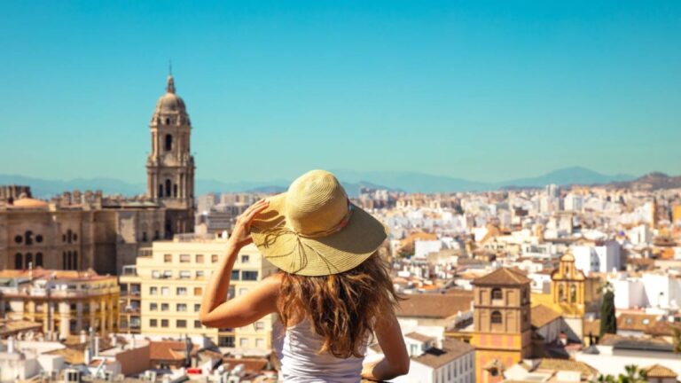 スペイン・マラガの街並みを眺める女性旅行者。麦わら帽子をかぶり、旧市街の歴史的建造物やカテドラルが広がる風景を見渡す爽やかな旅の一場面。