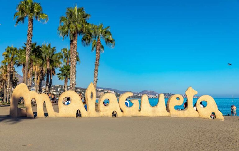 スペイン・マラガのマラゲータビーチにある有名な砂のモニュメント「Malagueta」のサイン。ヤシの木と青い空、地中海を背景にした人気のフォトスポット。