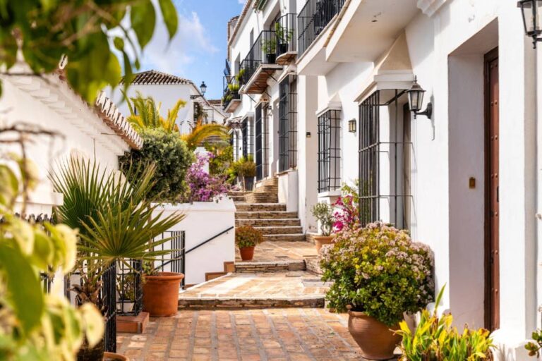スペイン・マラガ近郊の白い村にある階段状の石畳の路地。白壁の家々と色とりどりの鉢植えの花々が並び、穏やかで美しいアンダルシアの風景が広がる。