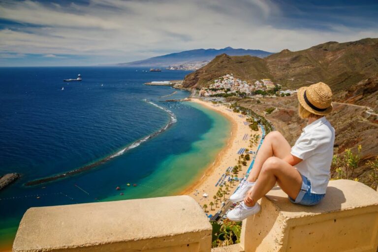 スペイン・テネリフェ島の人気スポット「ラス・テレシータス・ビーチ」を一望する女性旅行者。青く澄んだ海と金色の砂浜が広がる絶景の展望ポイント。