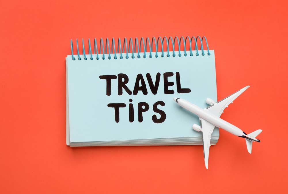 オレンジ色の背景に、青いリングノートに書かれた「TRAVEL TIPS」の文字と、飛行機のおもちゃが並ぶトラベルコンセプトのイメージ。