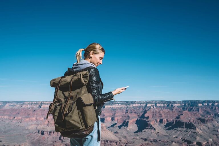 グランドキャニオンを背景にスマホを操作するアメリカ旅行中の女性