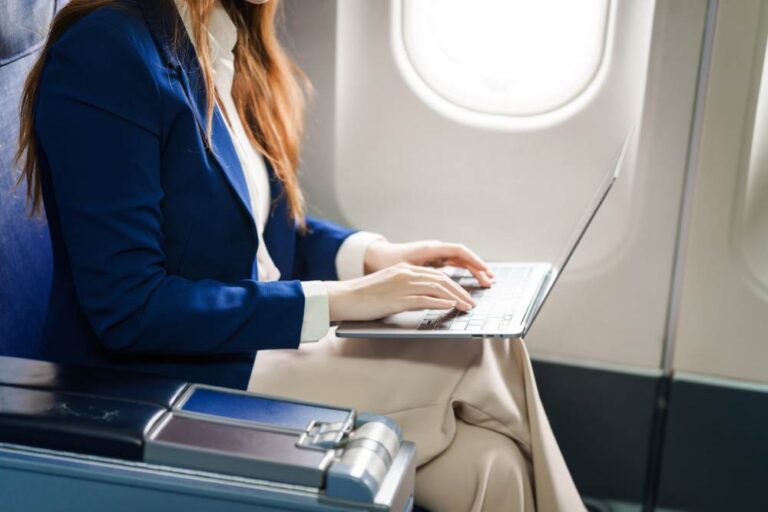 飛行機内でノートパソコンを使って仕事をするビジネスウーマン。出張中の移動時間を有効活用する様子。