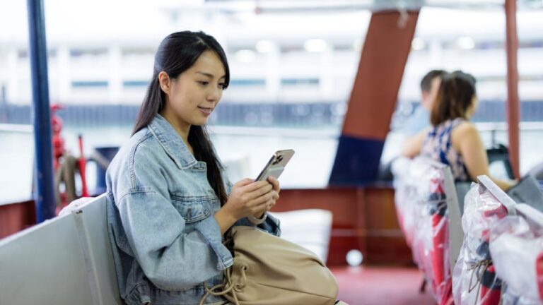 観光フェリーの座席でスマートフォンを操作する女性旅行者、カジュアルな装いでリラックスした様子。
