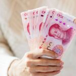 100元札の中国紙幣を扇状に広げて持つ人の手元。