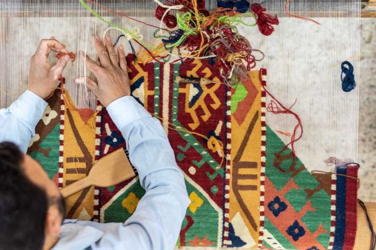 カラフルな伝統柄のカーペットを手織りするエジプトの職人。織り機に向かって細かな作業をする様子。