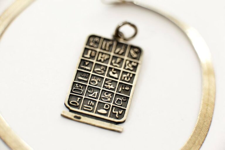 古代エジプトのヒエログリフが刻まれた四角形のシルバーペンダント。白背景の上に置かれている。