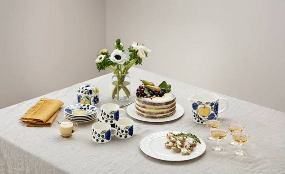フィンランドのアラビア製食器で彩られたテーブルコーディネート。フルーツケーキ、前菜、白い花、黄色のナプキンも並ぶ。