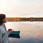 穏やかな湖畔でカヌーを背景にコーヒーを片手に佇む女性。自然豊かなフィンランドは治安が良く、静かな環境で安心して過ごせる旅行先として知られていることを象徴する一枚。