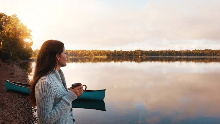 穏やかな湖畔でカヌーを背景にコーヒーを片手に佇む女性。自然豊かなフィンランドは治安が良く、静かな環境で安心して過ごせる旅行先として知られていることを象徴する一枚。