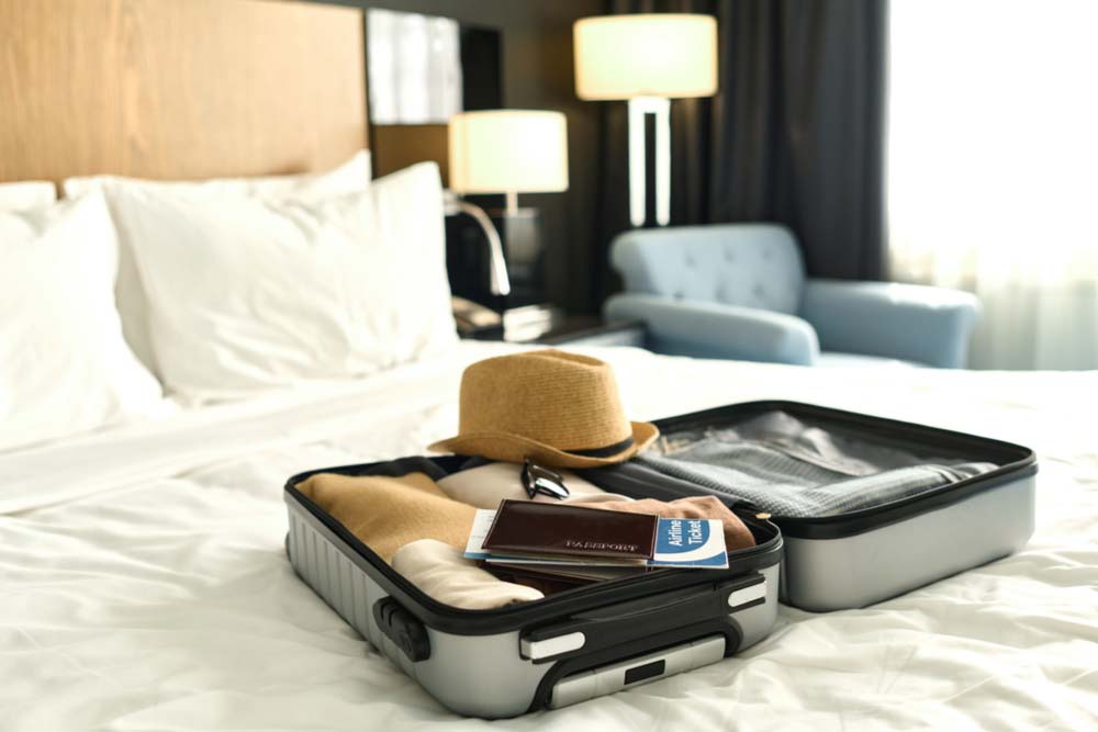ホテルのベッドに広げられたスーツケースと旅行アイテム。11月の海外旅行前に必要な服装や持ち物の準備を整えるシーン。