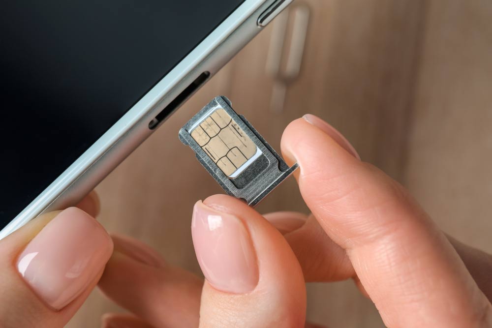 SIMカードをスマートフォンのSIMトレイに挿入する女性の手元のクローズアップ。携帯電話の設定や通信準備のイメージ。