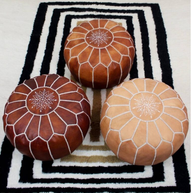 幾何学模様が刺繍された3色のモロッコ製レザープフ（オットマン）がラグの上に並べられている様子。
