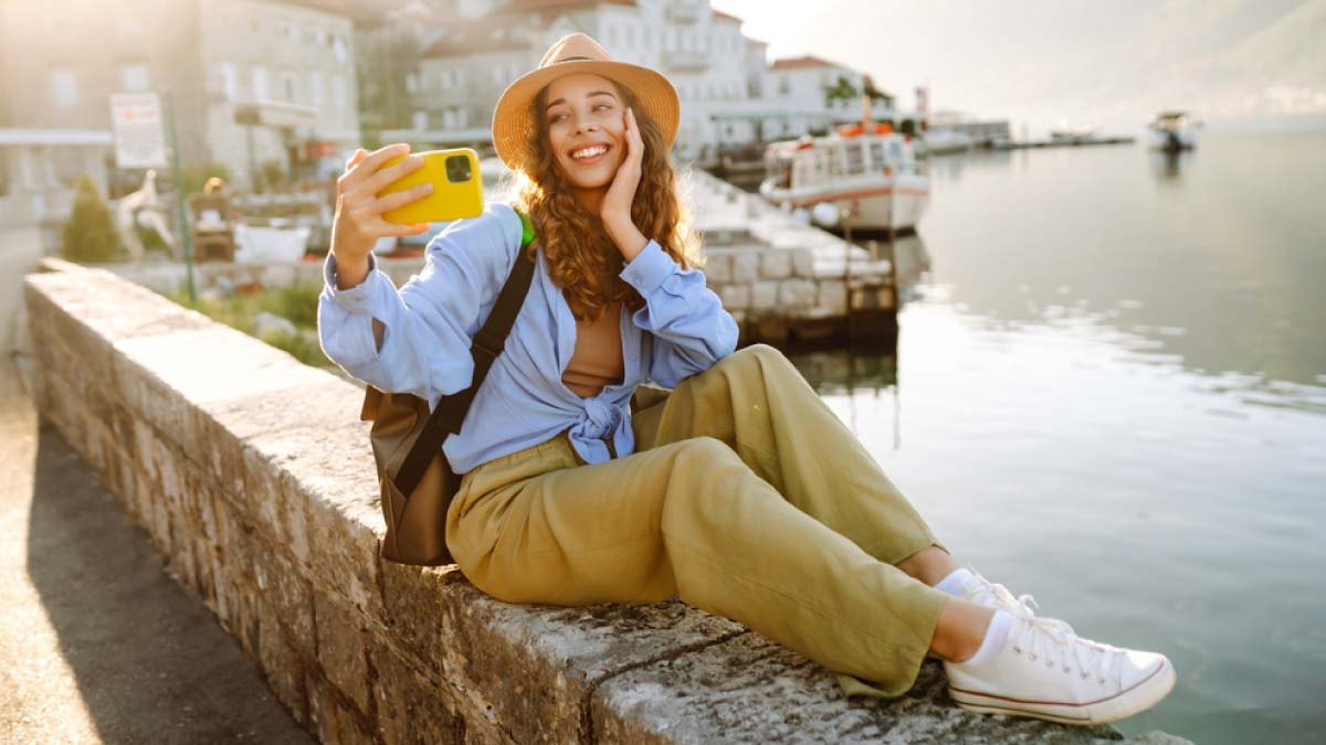 ヨーロッパの港町で自撮りを楽しむ女性旅行者。11月におすすめの海外旅行先で、絶景と街歩きを満喫する様子。