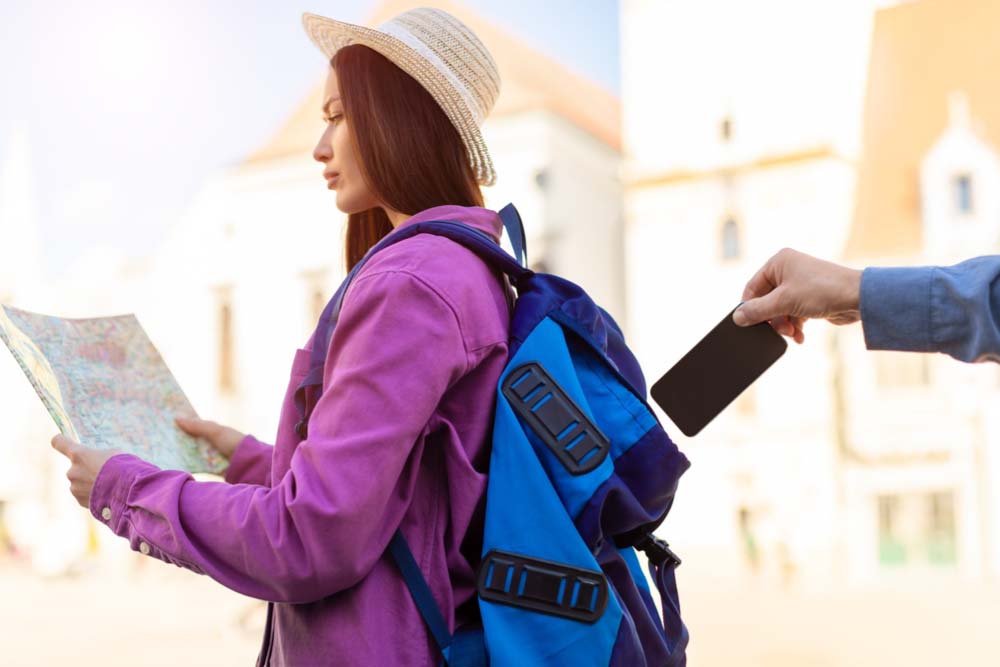 旅行中の女性が地図を見ている隙に、背後からスマートフォンを盗まれる瞬間。フィリピンなど海外旅行先で日本人が遭遇しやすいスリ被害の例として注意喚起に活用できる写真。