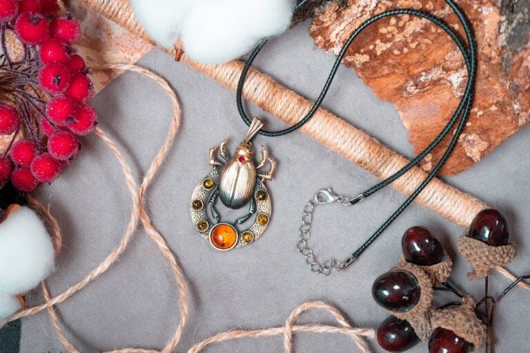 スカラベモチーフのアンバーストーン付きネックレスが、木の皮や綿、赤い実、ドングリなど秋らしい小物と共に並べられている。