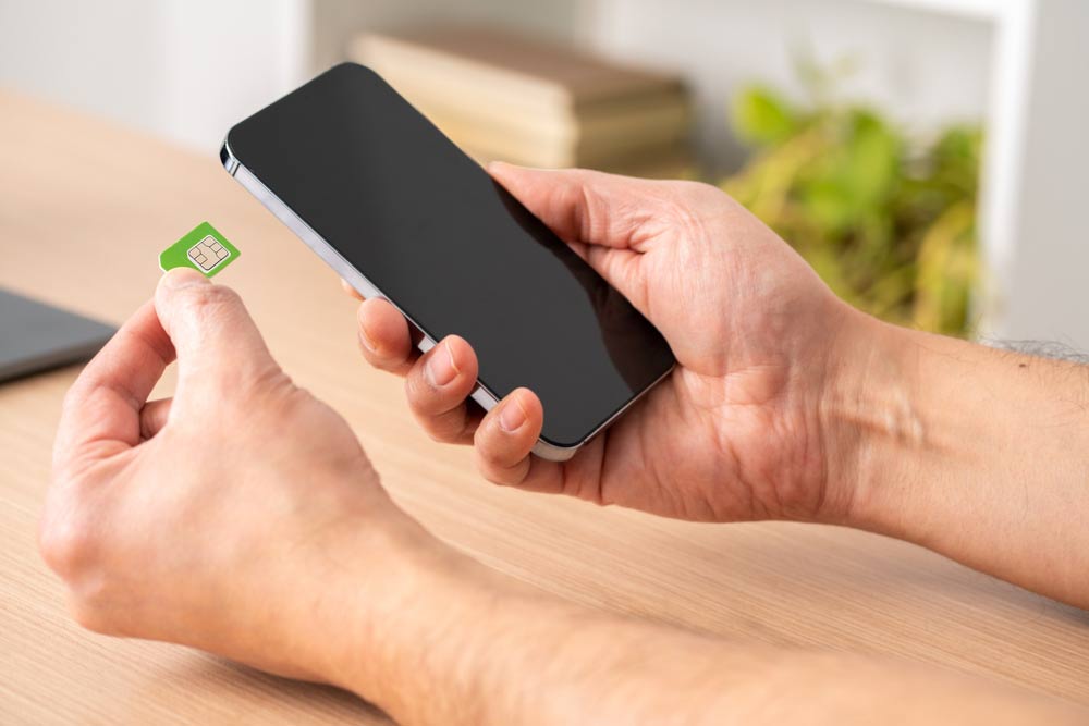 スマートフォンにSIMカードを挿入しようとしている手元の様子。デスクの上で行われており、背景には観葉植物が見える。
