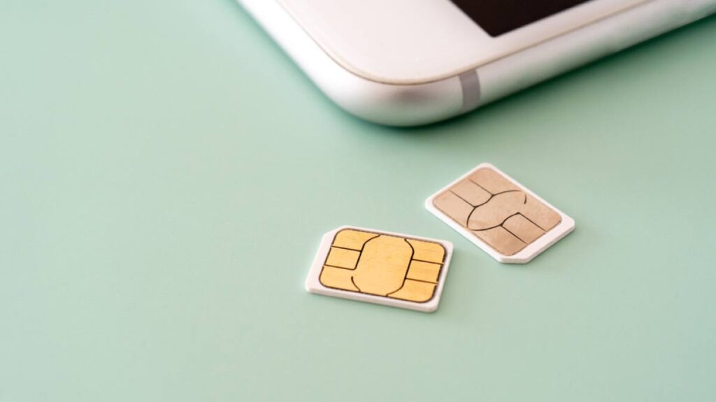 緑の背景の上に置かれた2枚のSIMカードとスマートフォンの一部。通信やモバイル端末に関するイメージ。