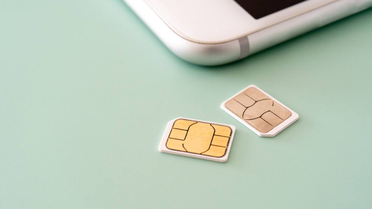 緑の背景の上に置かれた2枚のSIMカードとスマートフォンの一部。通信やモバイル端末に関するイメージ。