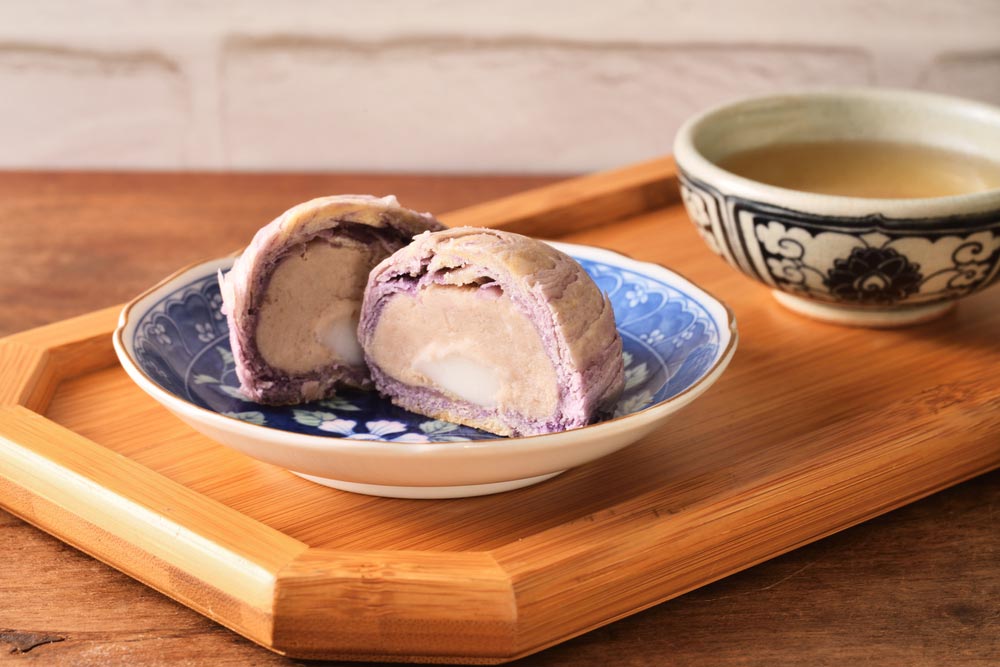 紫色のタロイモ餡がたっぷり詰まった台湾のタローパイが皿に盛られ、伝統的な茶器と一緒に並べられている様子。