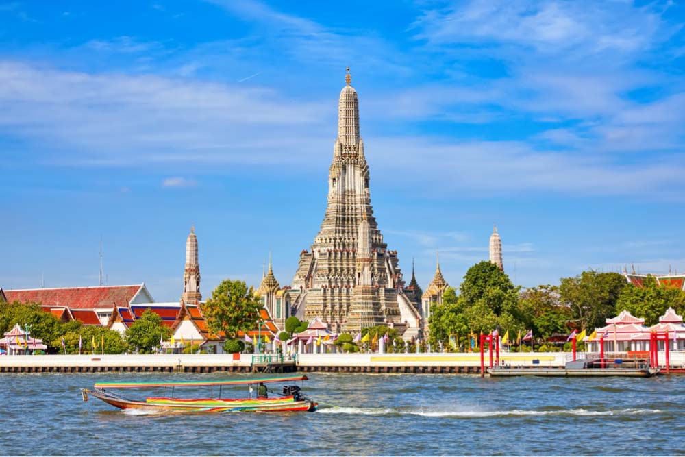タイ・バンコクのチャオプラヤー川越しに望むワット・アルン（暁の寺）とボートが行き交う風景