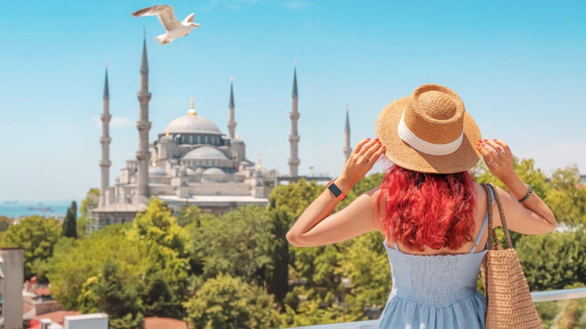 イスタンブールのブルーモスクを眺める女性観光客の後ろ姿。トルコ観光の魅力とともに、治安や安全対策を意識した旅の計画を促す記事に適した一枚。