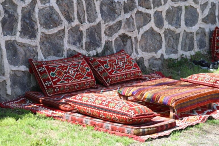 トルコの石壁のそばに敷かれた伝統的なキリムと色鮮やかなクッション。屋外に設けられた床座スタイルのリラックススペース。