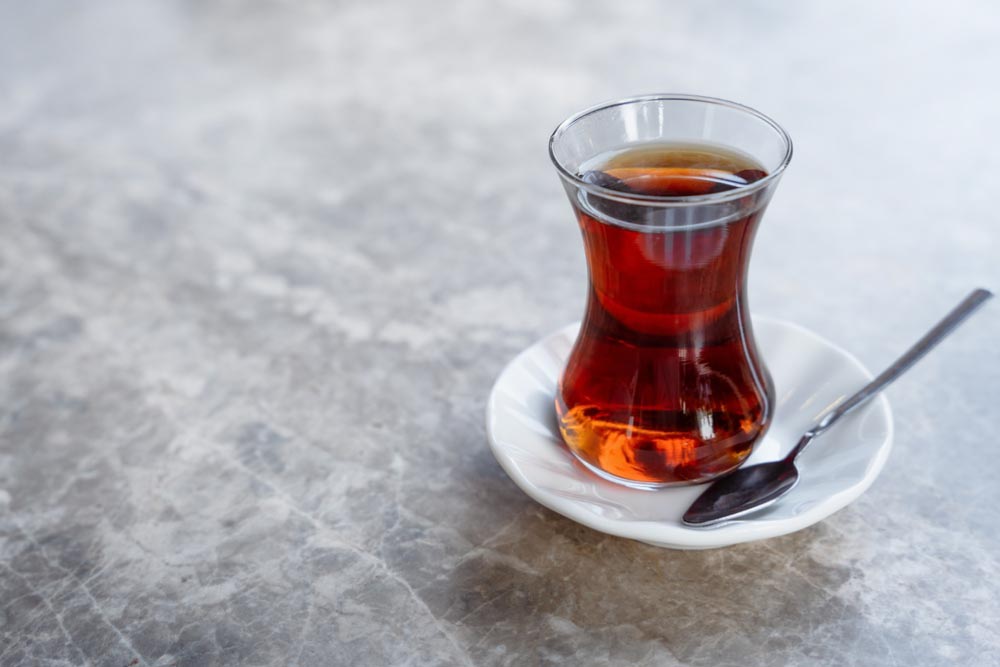トルコ式のチューリップ型グラスに注がれた紅茶が、白い受け皿とスプーンとともに大理石のテーブルに置かれている様子。