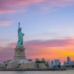 ニューヨークの夕焼け空を背景に立つ自由の女神と摩天楼の風景。