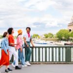 エッフェル塔を背景に、パリのセーヌ川沿いを笑顔で歩く4人の友人グループ。 Ask ChatGPT