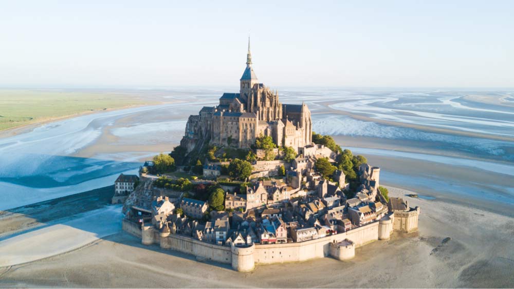 干潮時に広がる砂浜と潮の流れに囲まれたモン・サン・ミシェルの空撮ビュー