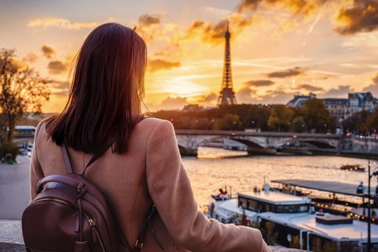 フランス・パリのセーヌ川沿いで、旅行者が夕暮れのエッフェル塔を眺めながら街歩きを楽しむ様子