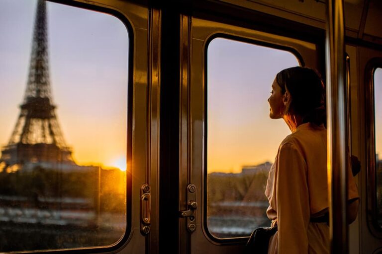 夕暮れのパリを電車の窓から眺める旅行者。10月の海外旅行で重ね着や羽織りを準備するイメージ