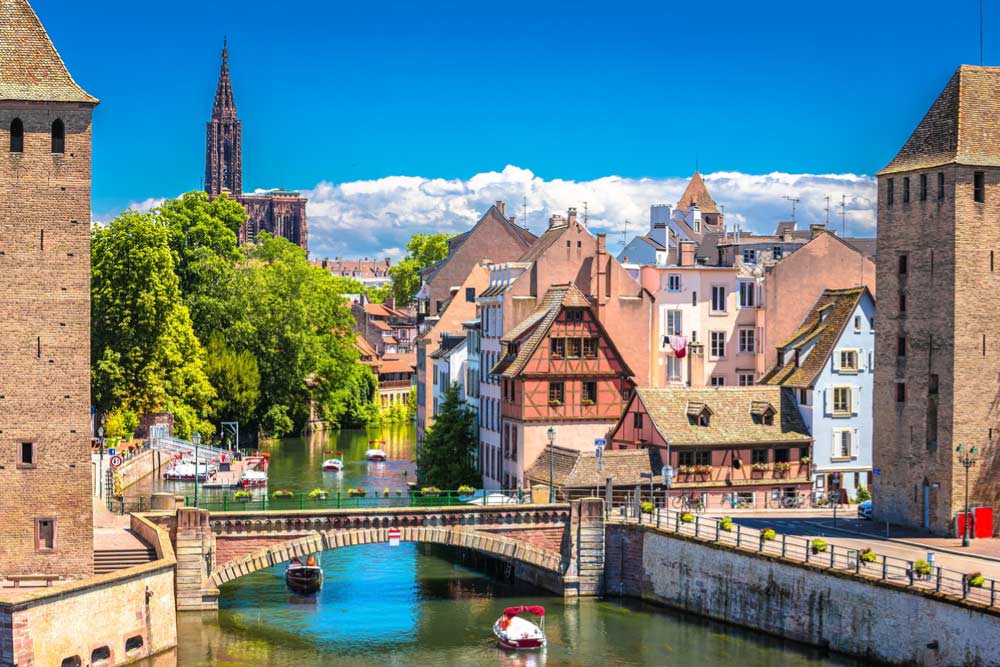 ストラスブールのプティット・フランス地区、運河沿いに並ぶ木組みの家と橋、背景にそびえるノートルダム大聖堂