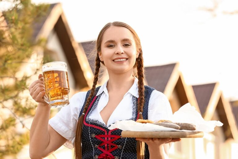 民族衣装の女性がビールジョッキと料理を持つ、ドイツ・ミュンヘンのオクトーバーフェストを楽しむ秋旅のイメージ