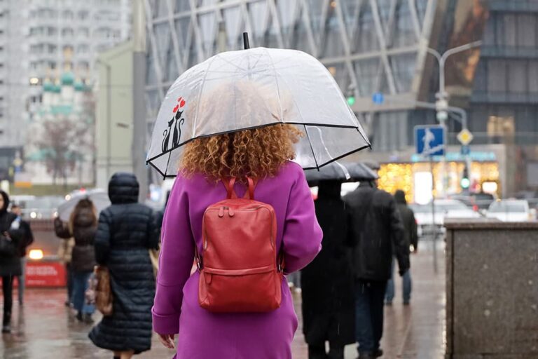 雨の街中を傘を差して歩く旅行者。10月の海外旅行で雨季や台風に備え、屋内プランを用意するイメージ