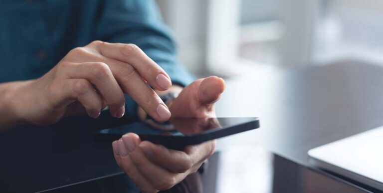 スマートフォンを操作する手元のクローズアップ。デスクの上で画面をタップしている様子。