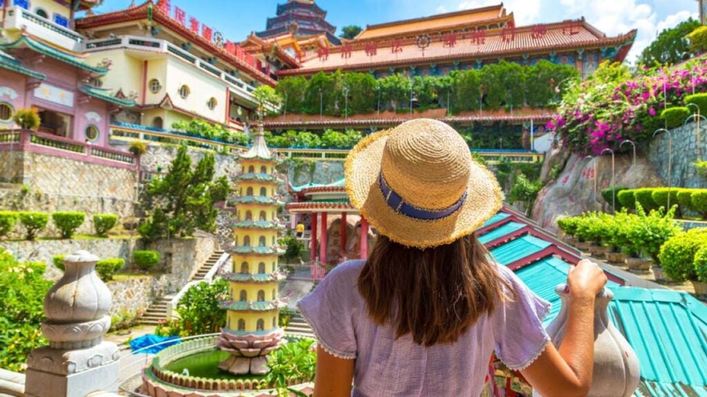 ストローハットをかぶった女性が、ペナンの極楽寺の色鮮やかな建物と庭園を見上げている後ろ姿.