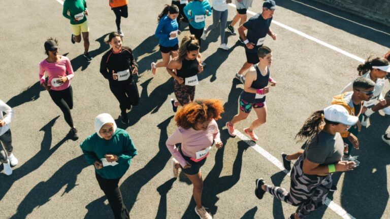ゼッケンを付けた多様なランナーたちが舗装道路を駆け抜けるマラソン大会の様子。