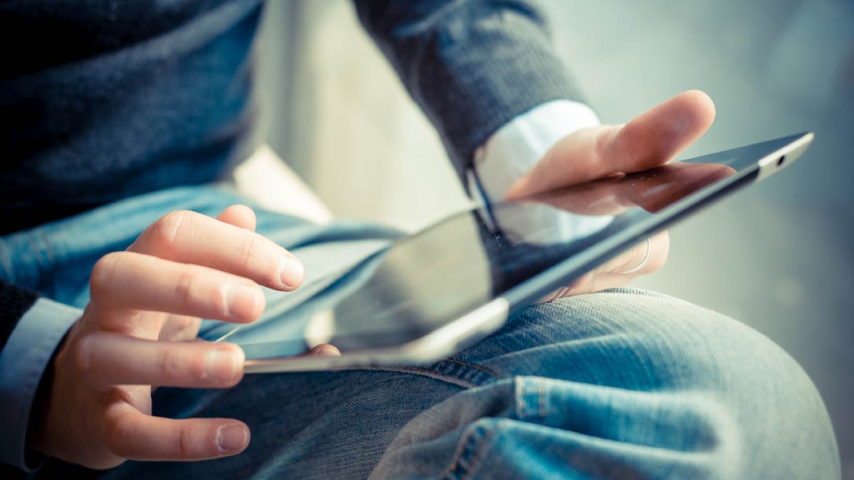 膝の上でタブレット端末を持ち、指で画面を操作する人の手元のクローズアップ。