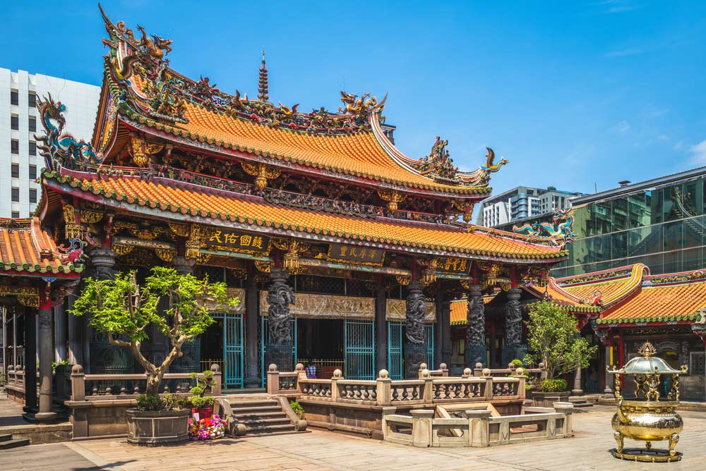 台北にある龍山寺の外観。鮮やかな朱色の屋根と精緻な装飾が施された歴史的な寺院が青空の下にそびえ立つ。