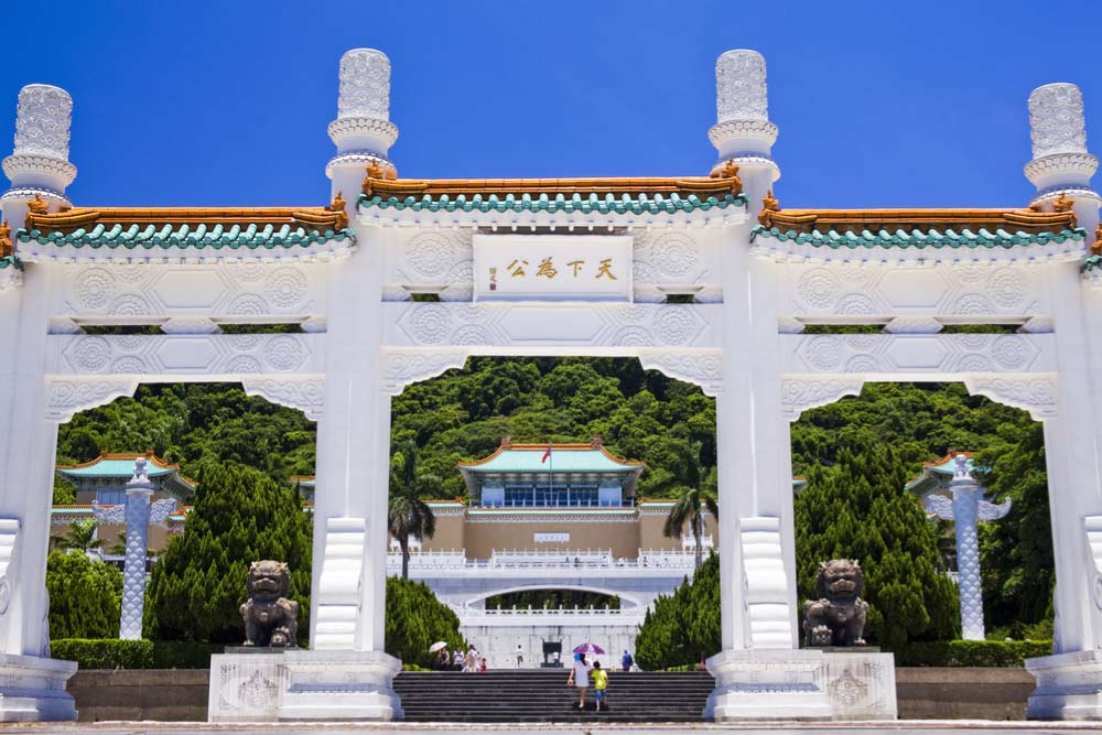 台北にある国立故宮博物院の正面ゲートと、その奥に見える緑の屋根の本館を青空の下で撮影した景観。