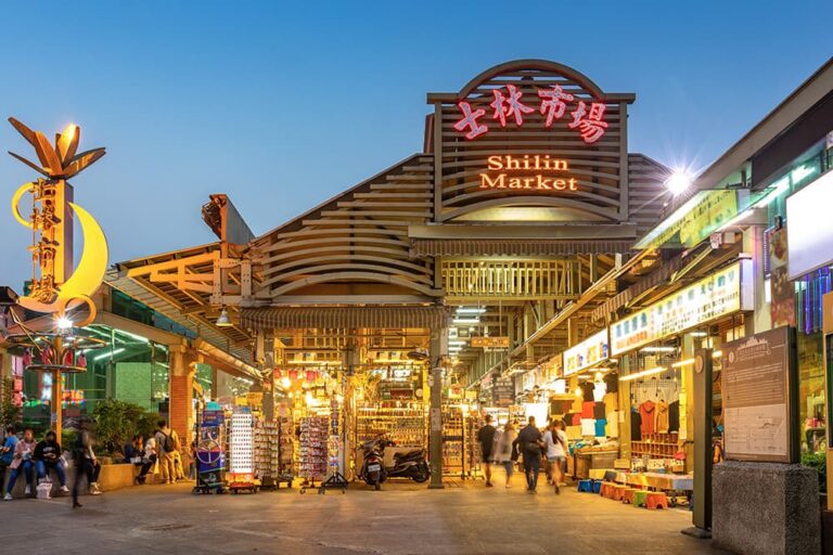 夜に明かりが灯る台北の士林市場入口と屋台街の様子。10月の台湾旅行で夜市グルメを楽しむイメージ