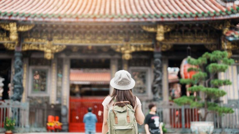 緑色のバックパックを背負った女性が台湾の歴史ある寺院を正面から眺めている。
