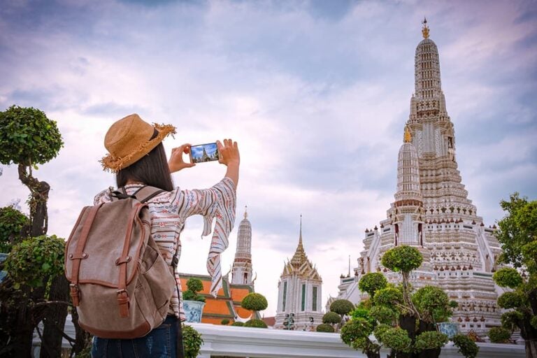 タイ・バンコクの寺院で、バックパックを背負った旅行者がスマートフォンで撮影を楽しむ様子